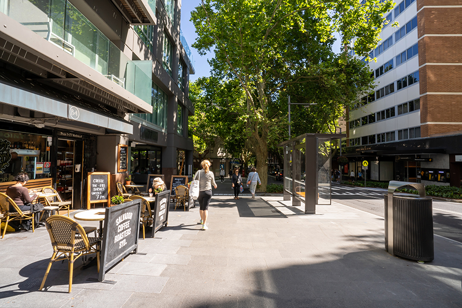Pedestrians walk between a café and bus stop on the new streetscape in Macleay Street, Potts Point.